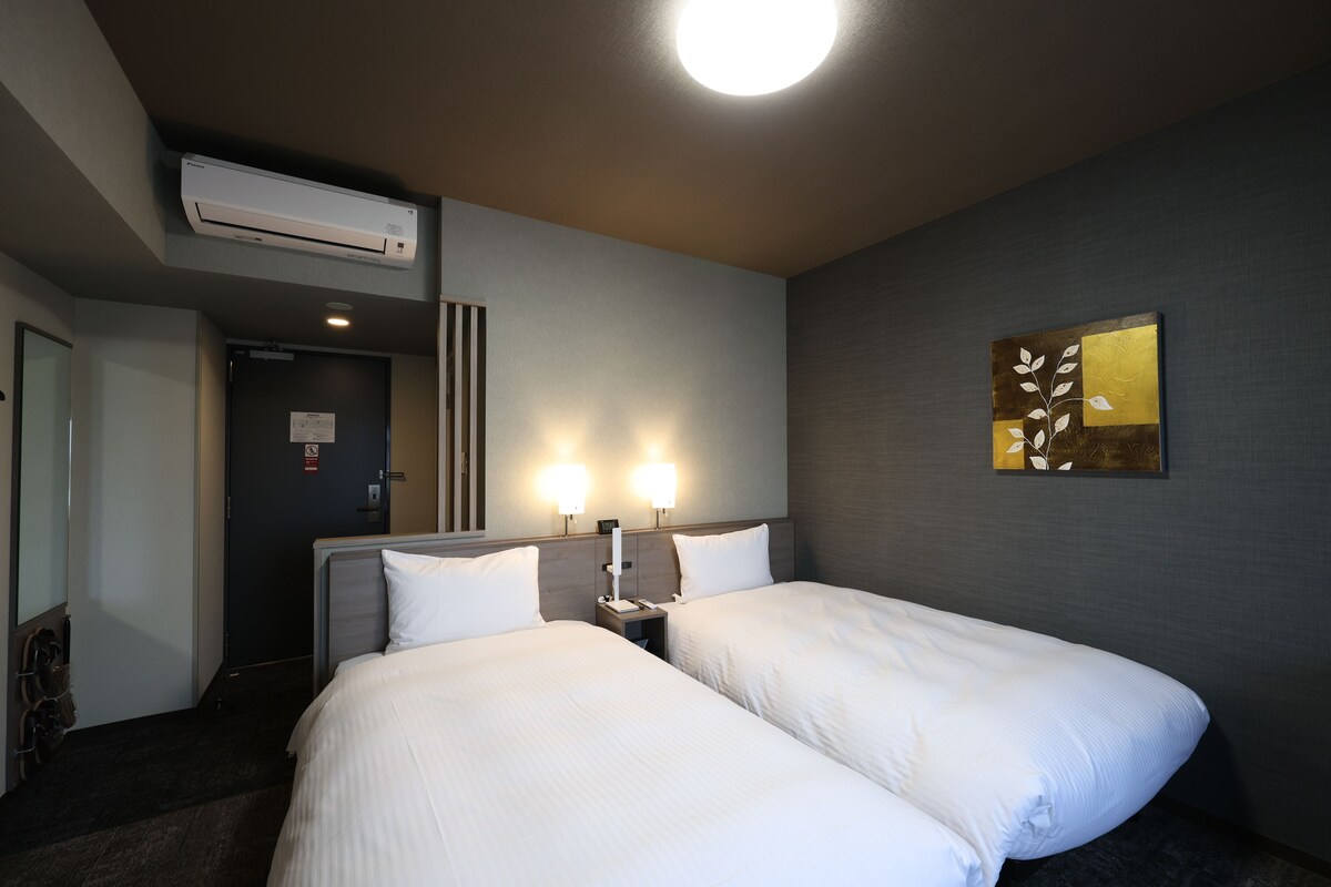 A hotel room with two beds, a wall-mounted air conditioner, and a painting.