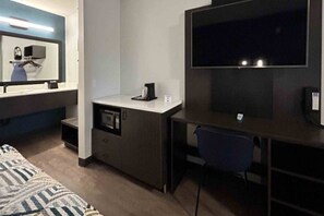 Una habitación de hotel compacta con una cama, un escritorio con una silla, un microondas y un televisor.