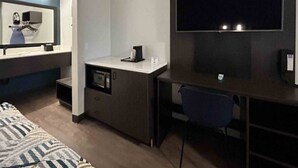 A compact hotel room with a bed, a desk with a chair, a microwave, and a television. - 1 King Bed | Non-Smoking, Micfridge (Lake Elsinore)