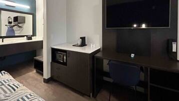 A compact hotel room with a bed, a desk with a chair, a microwave, and a television.