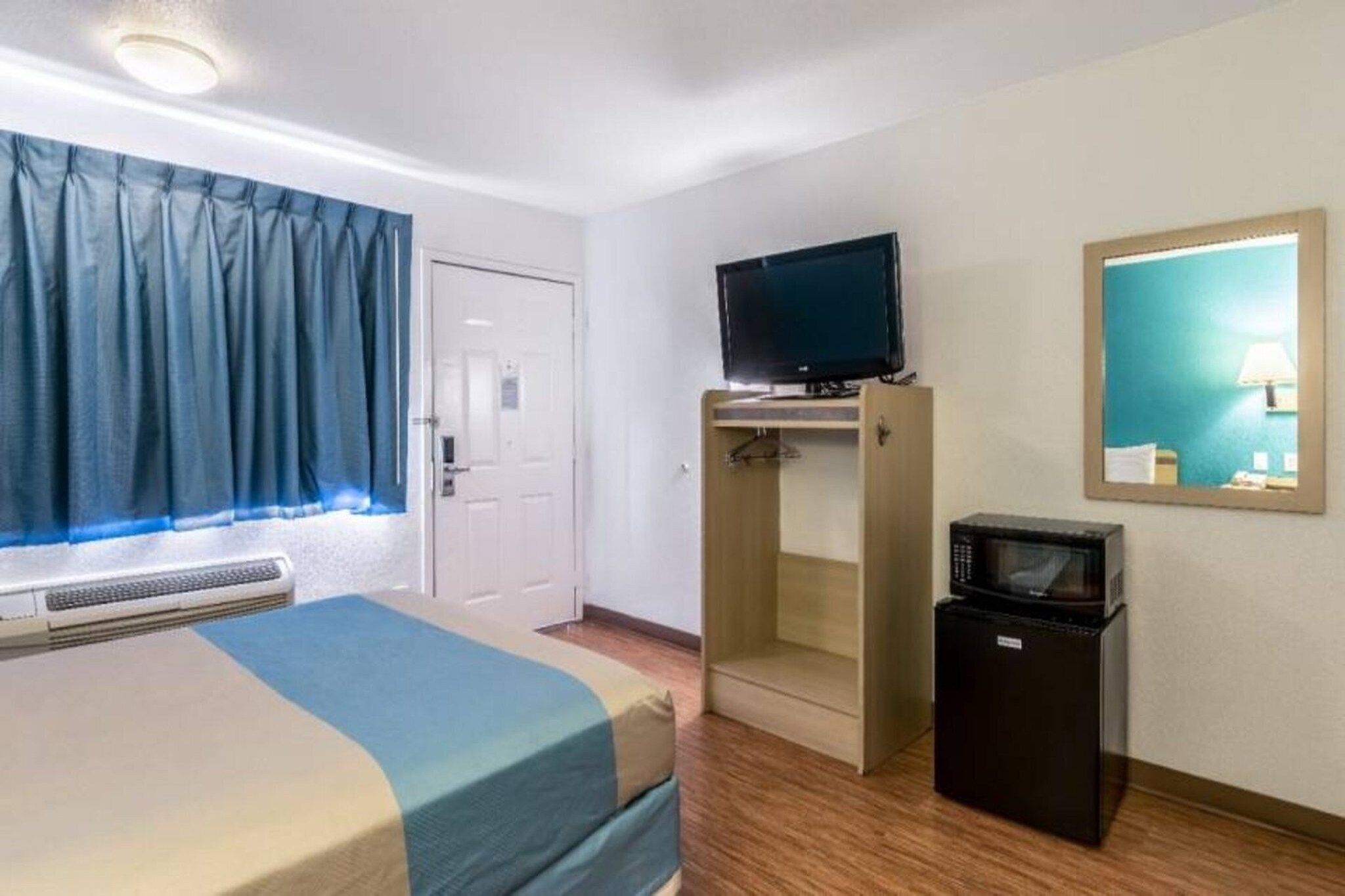 A hotel room with a bed, a television on a stand, a microwave, and a mirror on the wall.