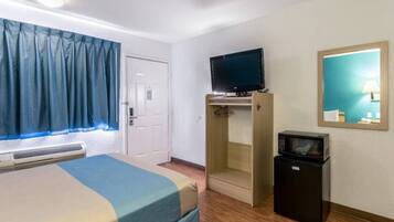 A hotel room with a bed, a television on a stand, a microwave, and a mirror on the wall.