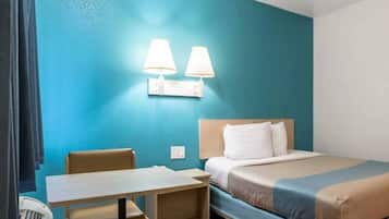 Habitación de hotel con cama, una mesa, dos lámparas de pared y un ventanal con cortinas.