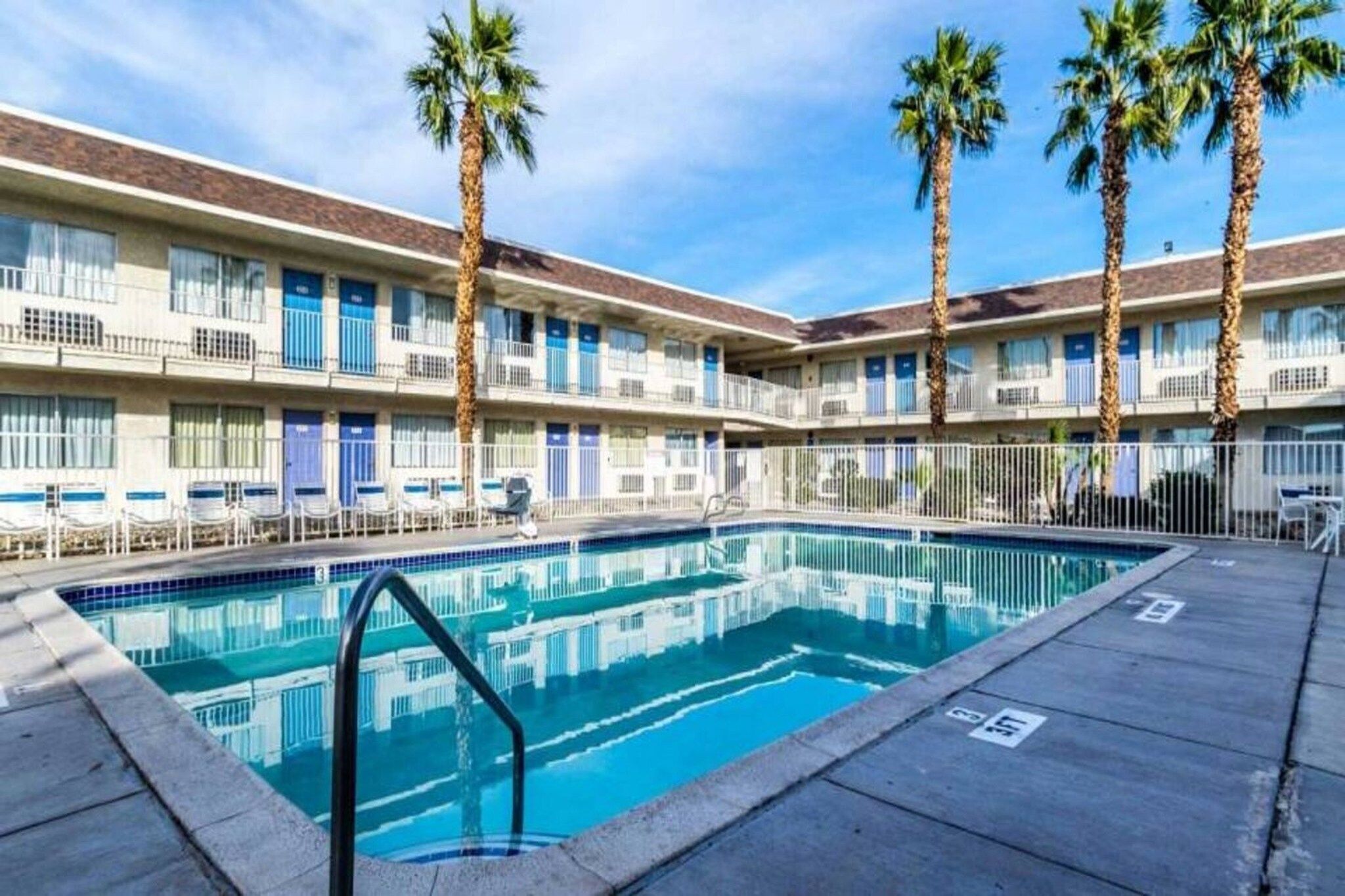 A hotel with a swimming pool, palm trees, and a two-story building with balconies.