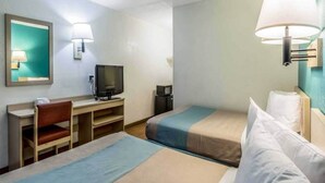 Ein Hotelzimmer mit Schreibtisch, Fernseher, zwei Betten und einem Sessel.