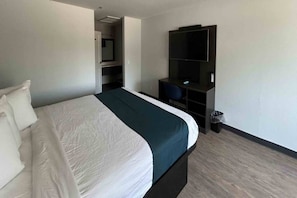 Habitación de hotel con cama, escritorio, silla, televisor y cubo de basura.