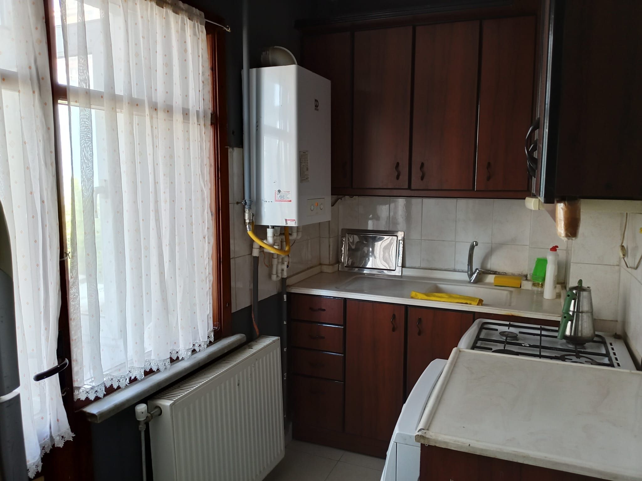 Una cocina compacta con estufa integrada, un lavamanos y un ventanal con cortinas.