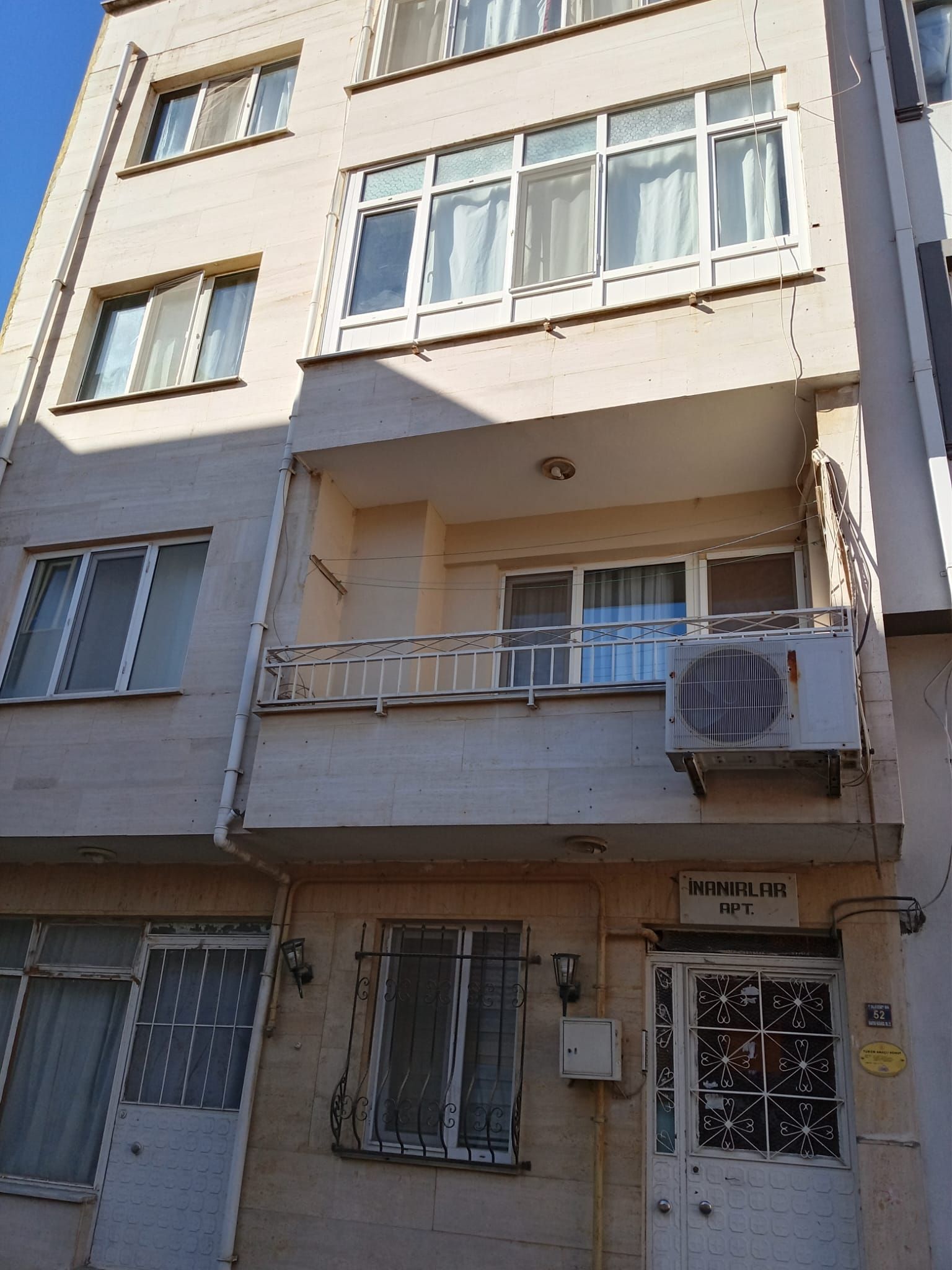 A multi-story building with balconies, a sign indicating 'INANILAR APT.', and a window with decorative metalwork.