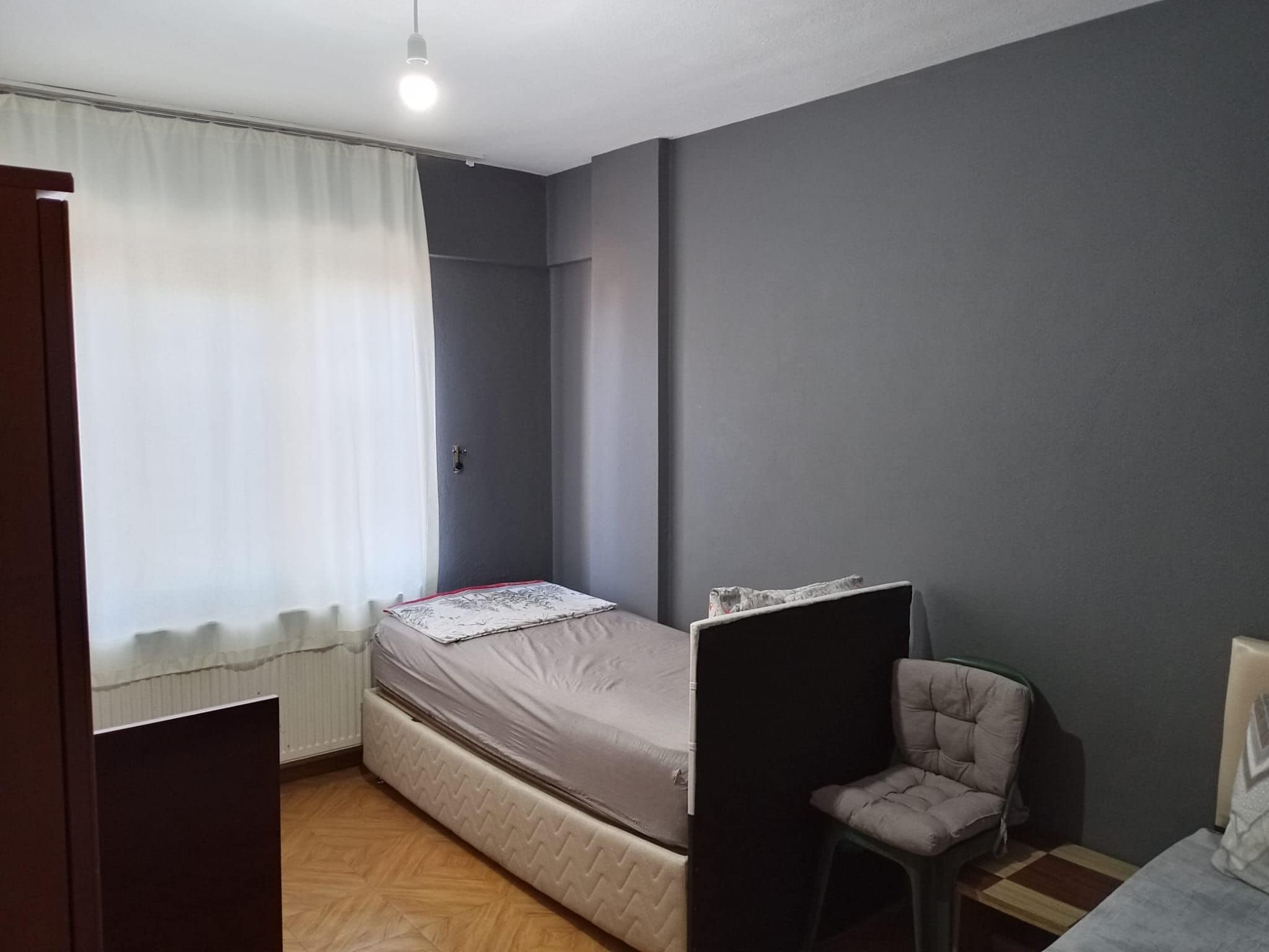 Une petite pièce, peu meublée, avec un lit simple, une chaise et un radiateur.