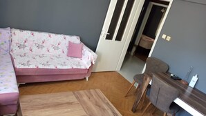 Ein Zimmer mit einer Couch, einem Holztisch, einem Schreibtisch mit Stuhl und einer Tür zu einem weiteren Raum.