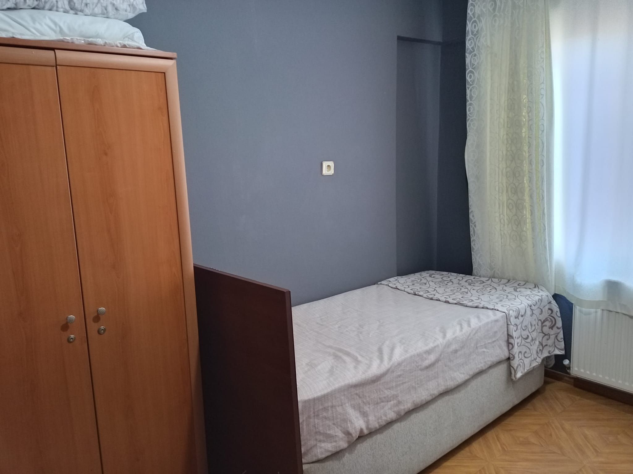 Una habitación con una cama individual, un armario y una ventana con cortinas.