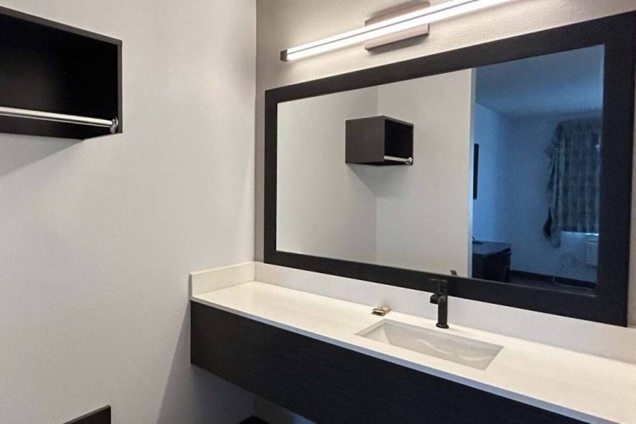 A modern bathroom with a large mirror, a white sink, and a dark countertop.