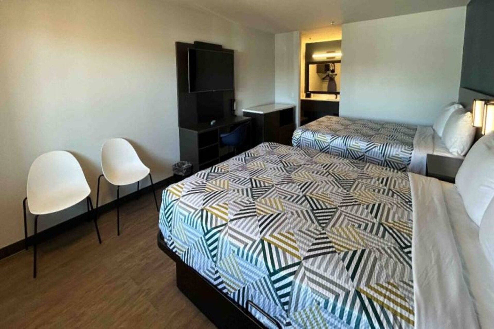 Hotellihuone, jossa on kaksi sänkyä, työpöytä, tuoli, televisio ja pieni kylpyhuone.