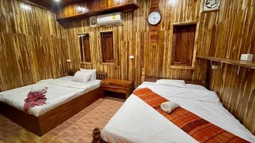 A room with two wooden beds, a wooden floor, a wall clock, and a ceiling fan.