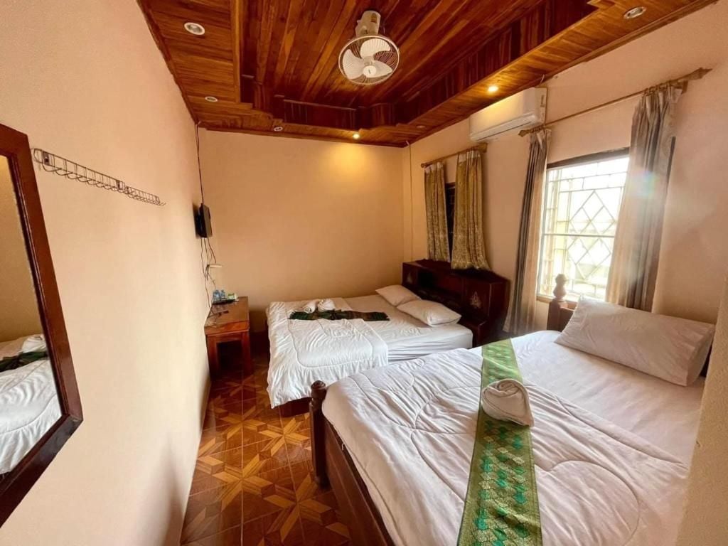 Habitación de hotel con dos camas, techo de madera, un ventilador y una ventana con cortinas.