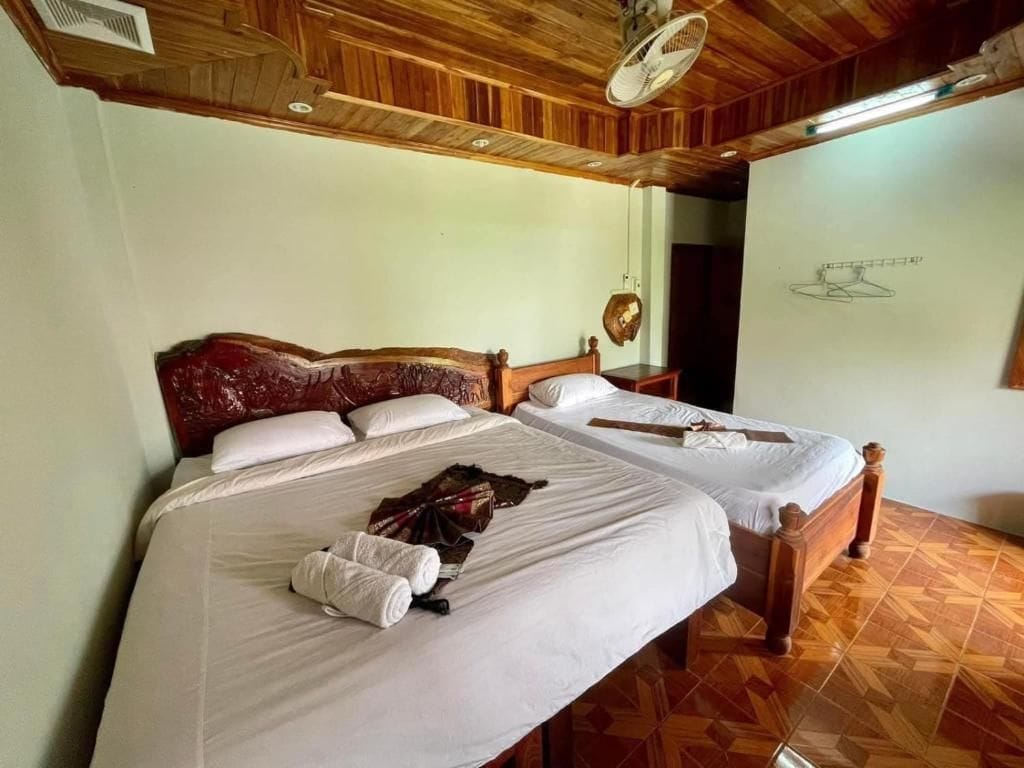 A hotel room with two beds, wooden headboards, a ceiling fan, and a patterned floor.