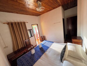 Habitació d'hotel amb sostre de fusta, un llit amb mantell de llit de disseny blau, una nitrera de fusta i una finestra amb cortines.