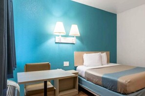 Habitación de hotel con cama, una mesa, dos lámparas de pared y un ventanal con cortinas.