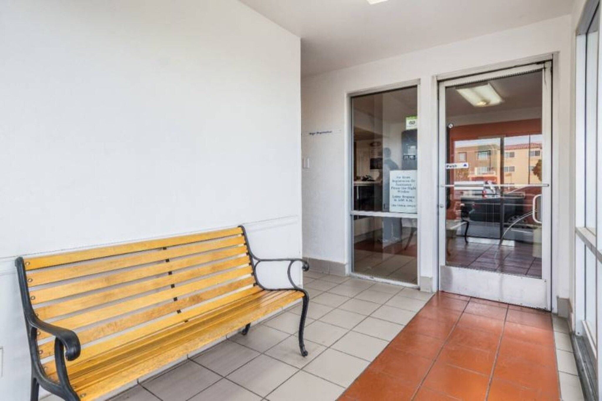 A bench in a hallway with a tiled floor and a glass door leading to an outdoor area.