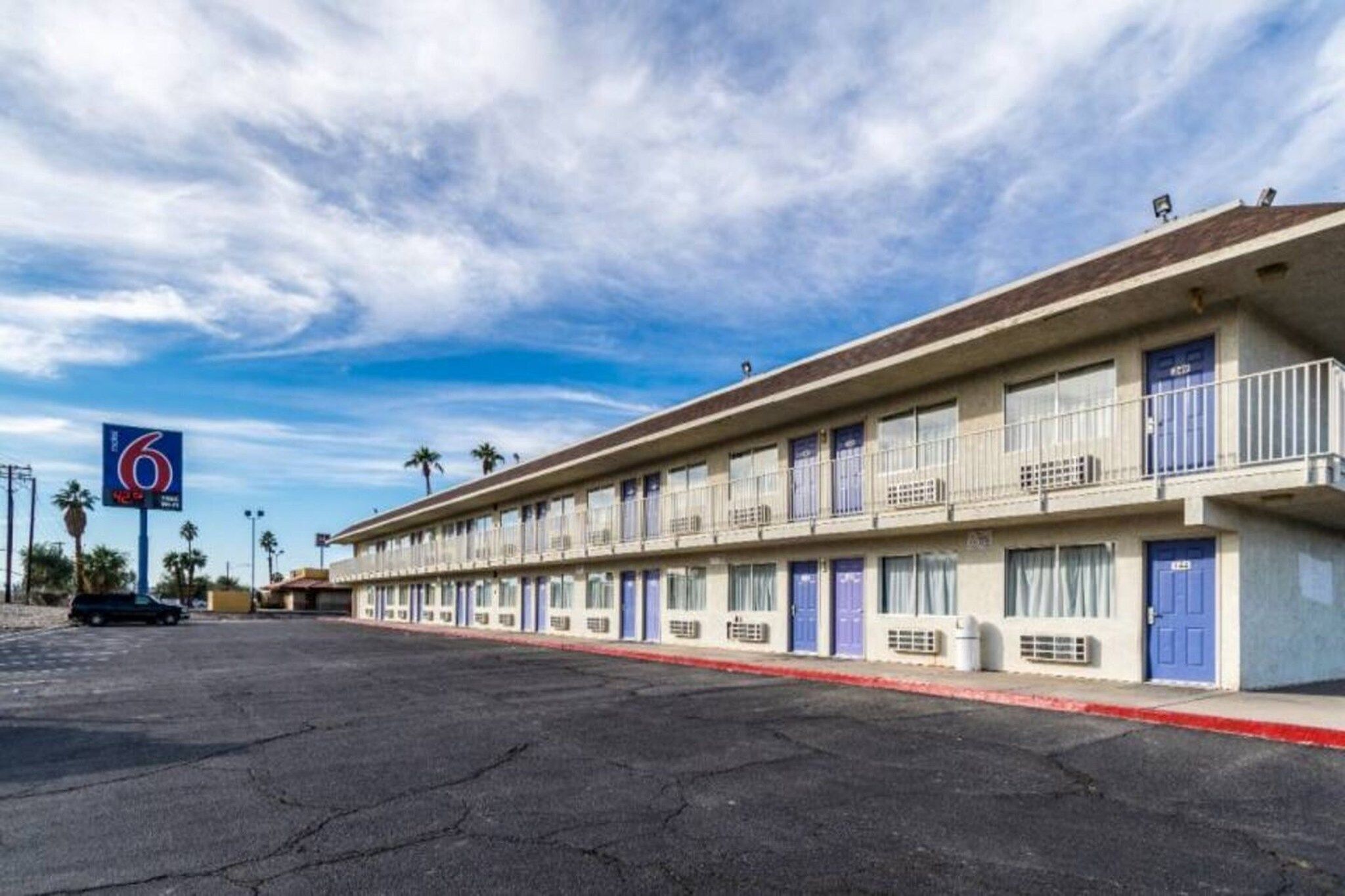 A motel with a row of rooms, a parking lot, and a clear sky.