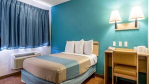 Ein Hotelzimmer mit einem Bett, einem Schreibtisch, zwei Lampen und einem Fenster mit Vorhängen.