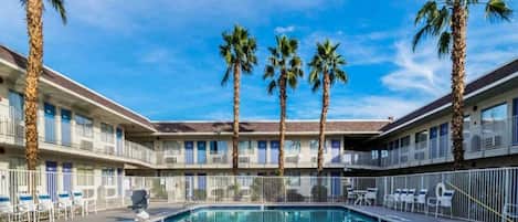 A hotel with a swimming pool, palm trees, and a clear sky.