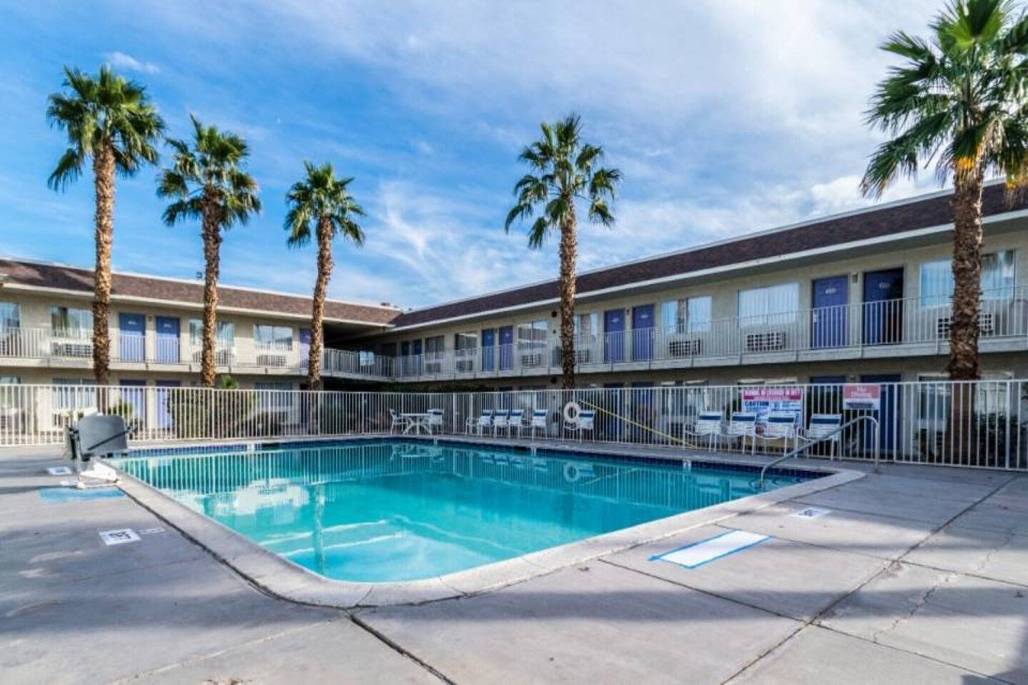Ein Hotel mit Swimmingpool, Palmen und einem eingezäunten Deckbereich.