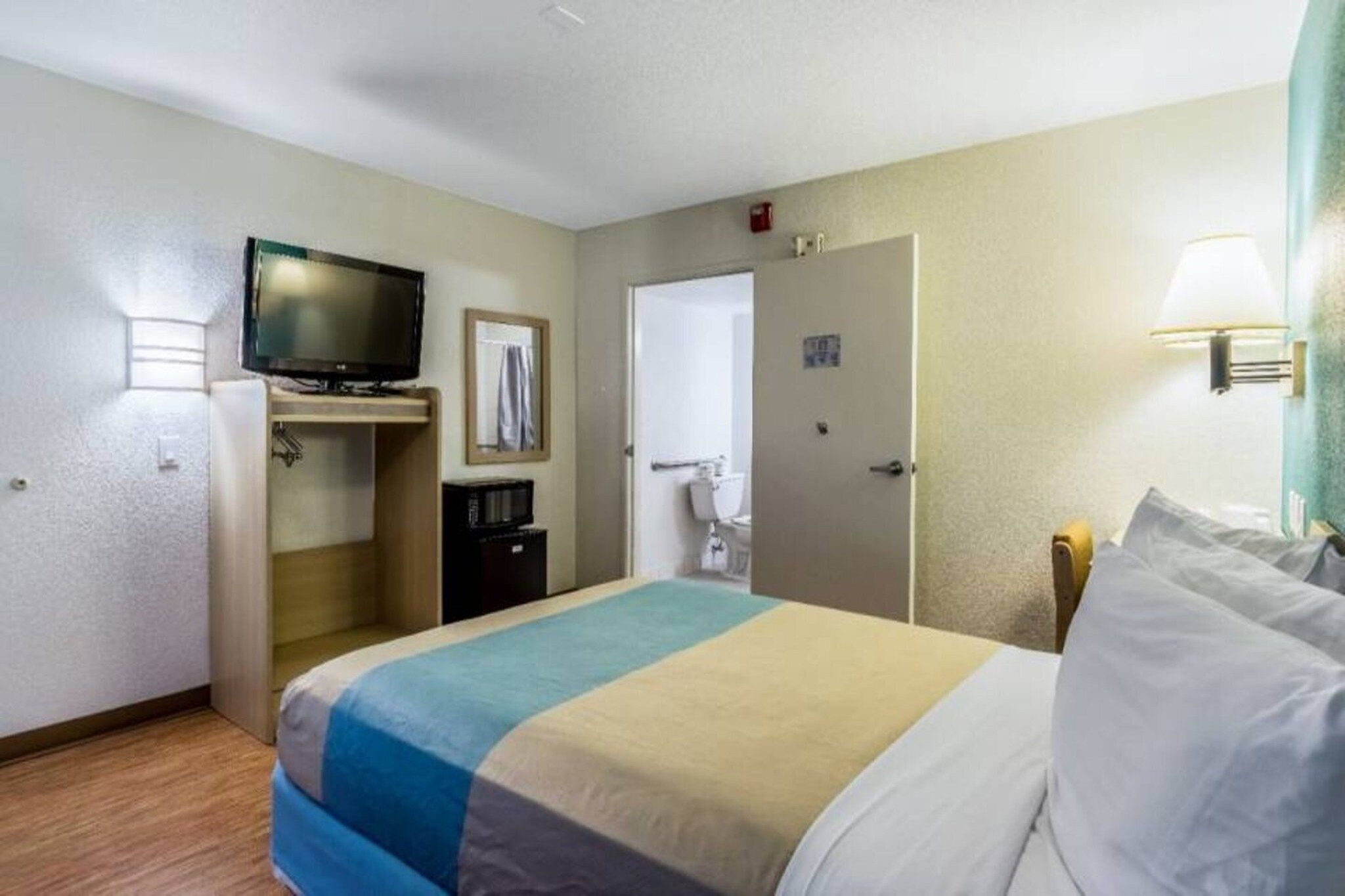 Una habitación de hotel con una cama, televisión, microondas, puerta y lámpara.
