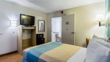 Una habitación de hotel con una cama, televisión, microondas, puerta y lámpara.