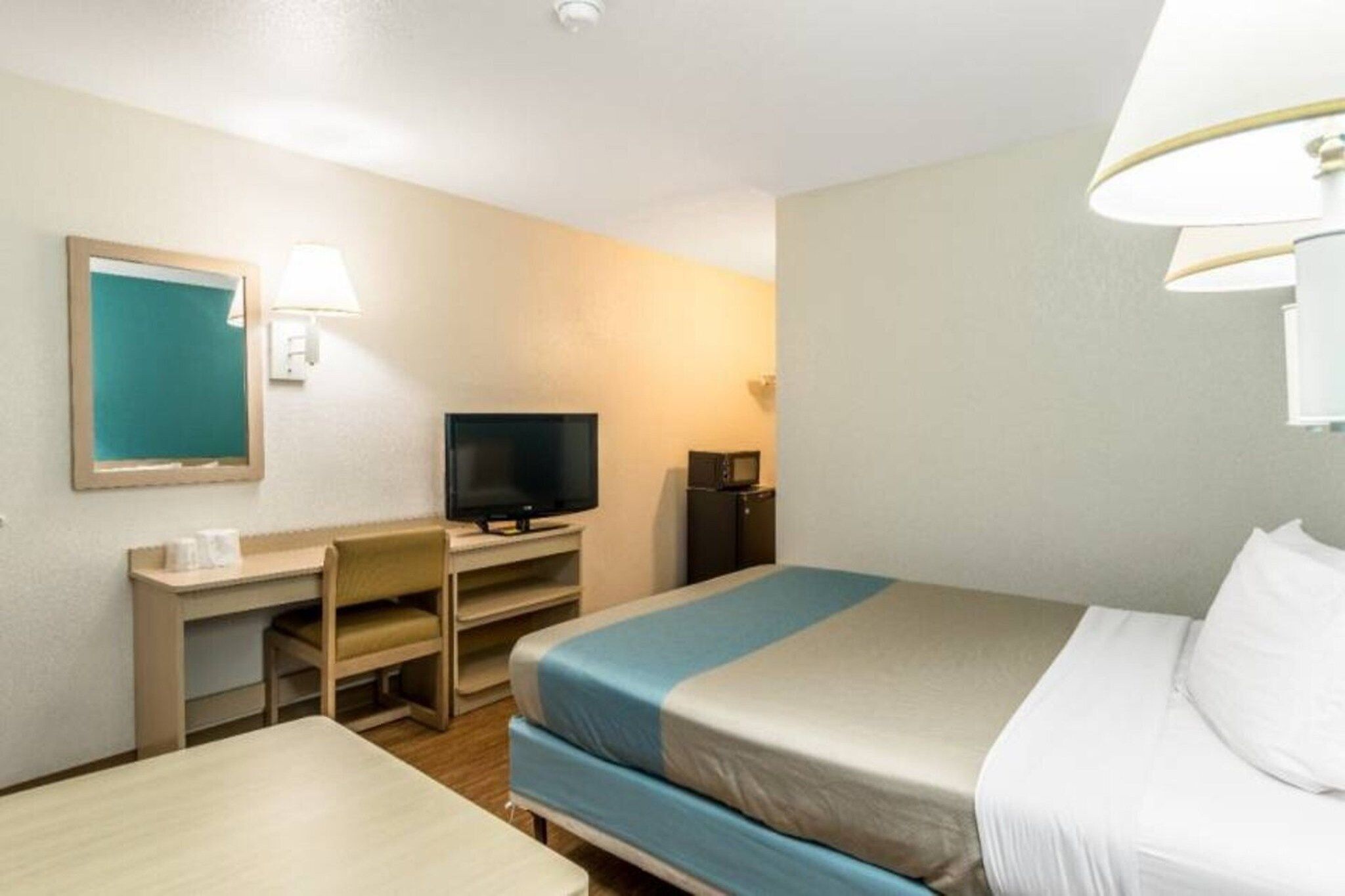 Ein Hotelzimmer mit Bett, Schreibtisch, Stuhl, Fernseher und Lampe.