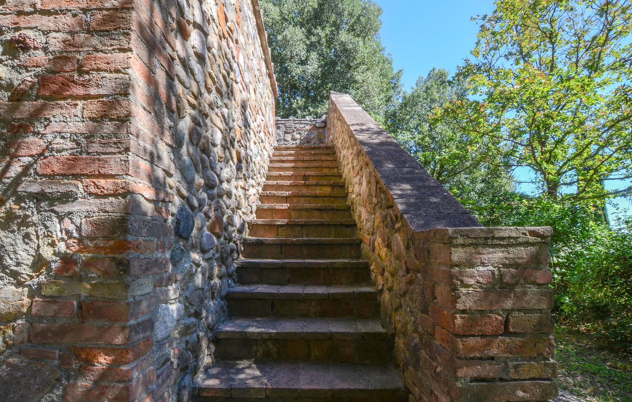 Un escalier en pierre menant au sommet d’une colline, entouré d’arbres et sous un ciel dégagé.
