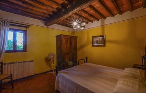 Ein Zimmer mit Bett, einem Vorhangfenster, einem Heizkörper, einem Holzschrank und einem Bild an der Wand.