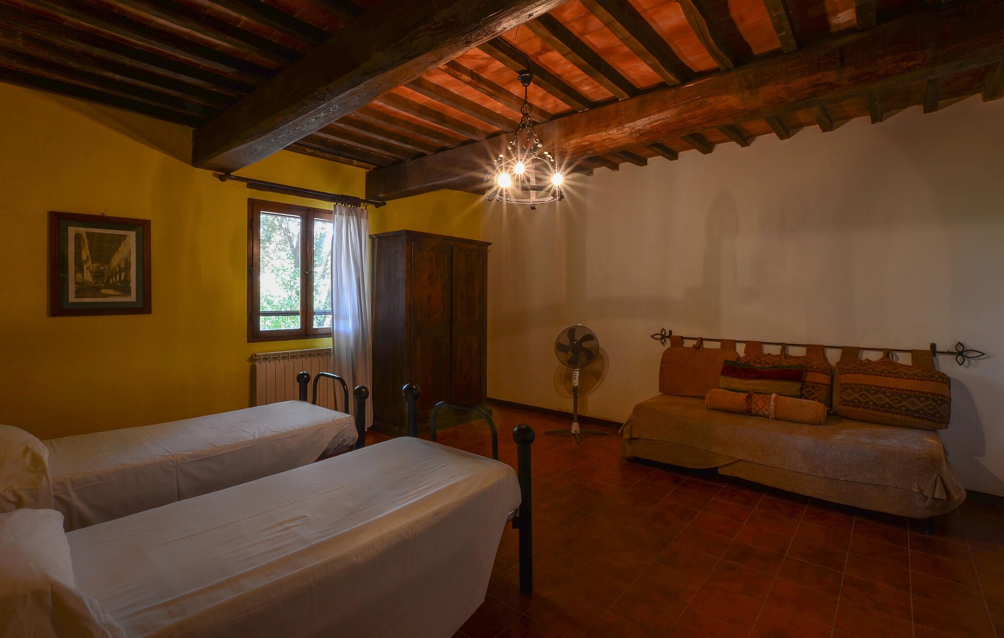 Une chambre avec deux lits, un plafond en bois, une fenêtre avec des rideaux, un radiateur, un ventilateur et un canapé.