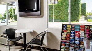 Habitación con televisor de pantalla plana montado en la pared, dos sillas negras alrededor de una pequeña mesa blanca y una ventana con vistas a un seto exterior.