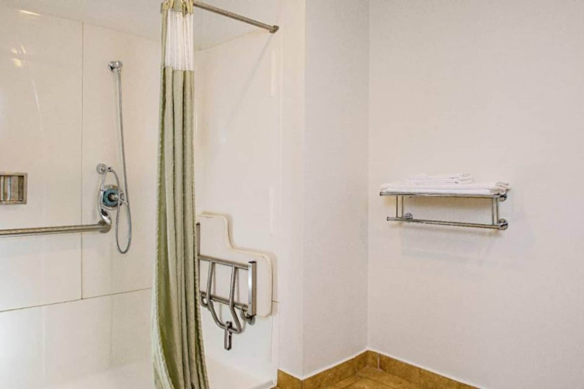 Une salle de bain équipée d’une douche, de barres d’appui, d’un porte-serviettes et d’un support à papier toilette.
