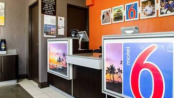 A motel reception desk with a large '6' sign, a computer, and a poster with a sunset and palm trees.