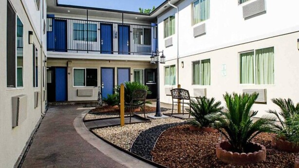 Un patio con un edificio que tiene balcones, una zona de estar con sillas y plantas en macetas.