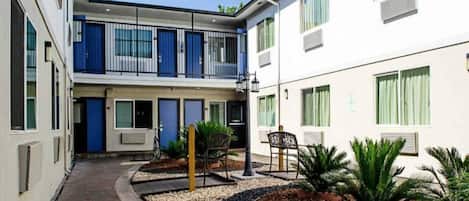 Une cour intérieure avec un bâtiment doté de balcons, un espace aménagé avec des chaises et des plantes en pot.