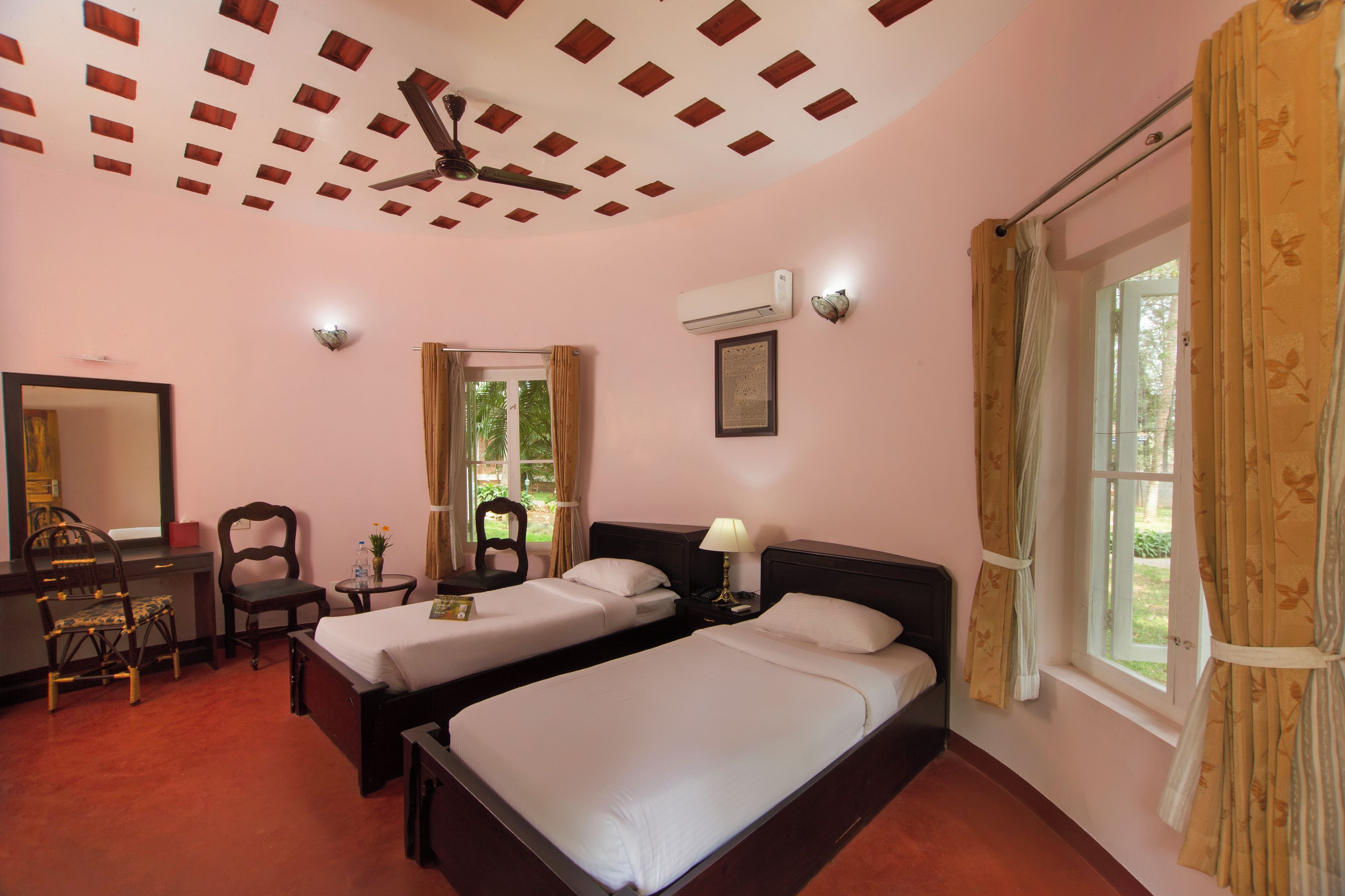 Une chambre d’hôtel avec deux lits, un bureau, une chaise, un ventilateur de plafond, un appareil de climatisation et une fenêtre avec des rideaux.