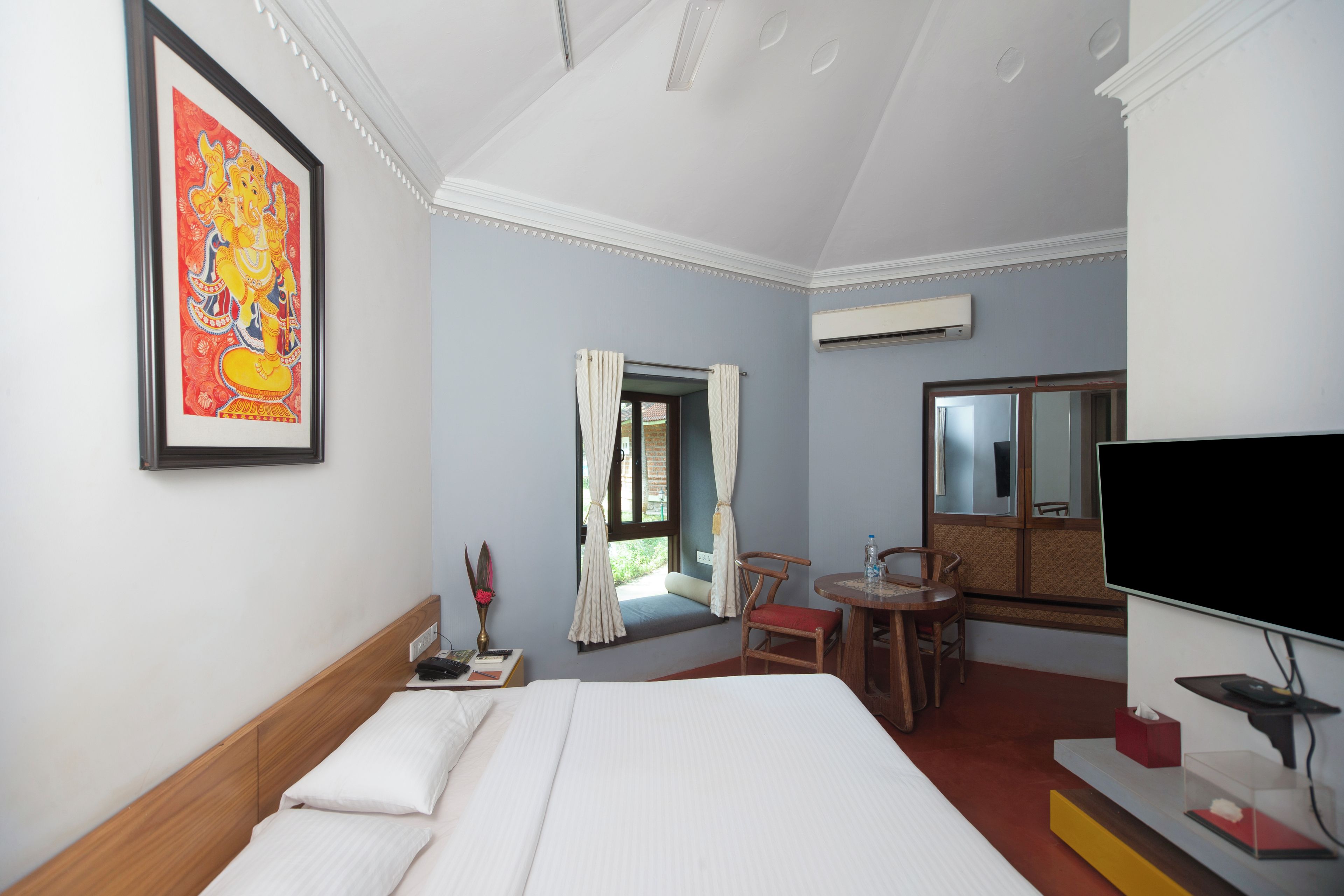 A hotel room with a bed, a desk with a chair, a television, and a window with curtains.