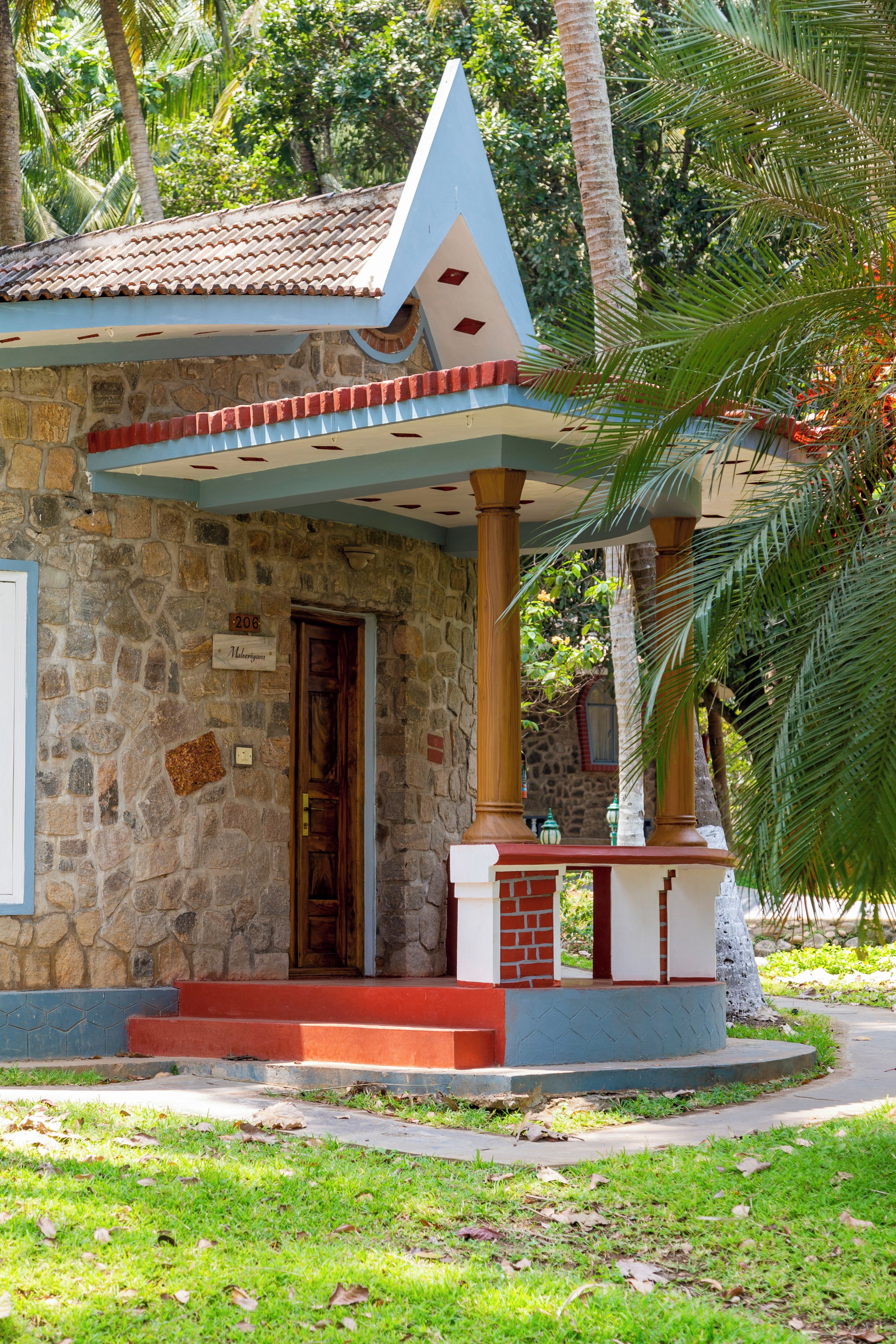Un edificio de piedra con techo de tejas, una puerta de madera y un pequeño porche con barandilla roja y blanca.
