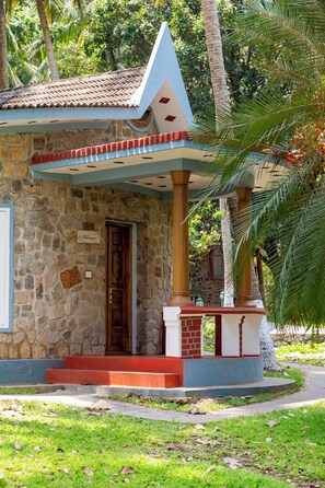 A stone building with a tiled roof, a wooden door, and a small porch with a red and white railing.