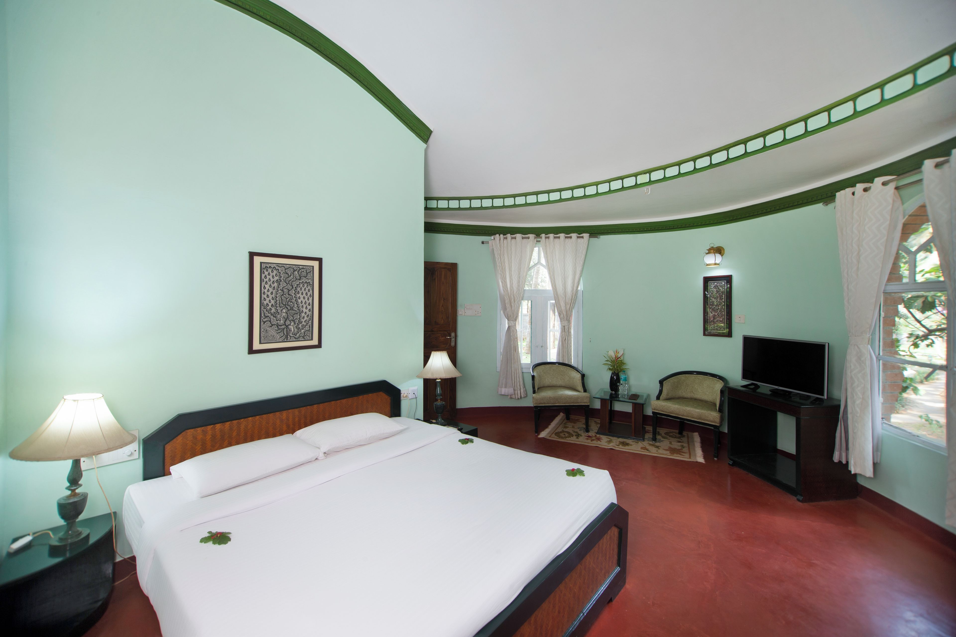 Een hotelkamer met een bed, een televisie, een stoel, een klein tafeltje en een raam met gordijnen.