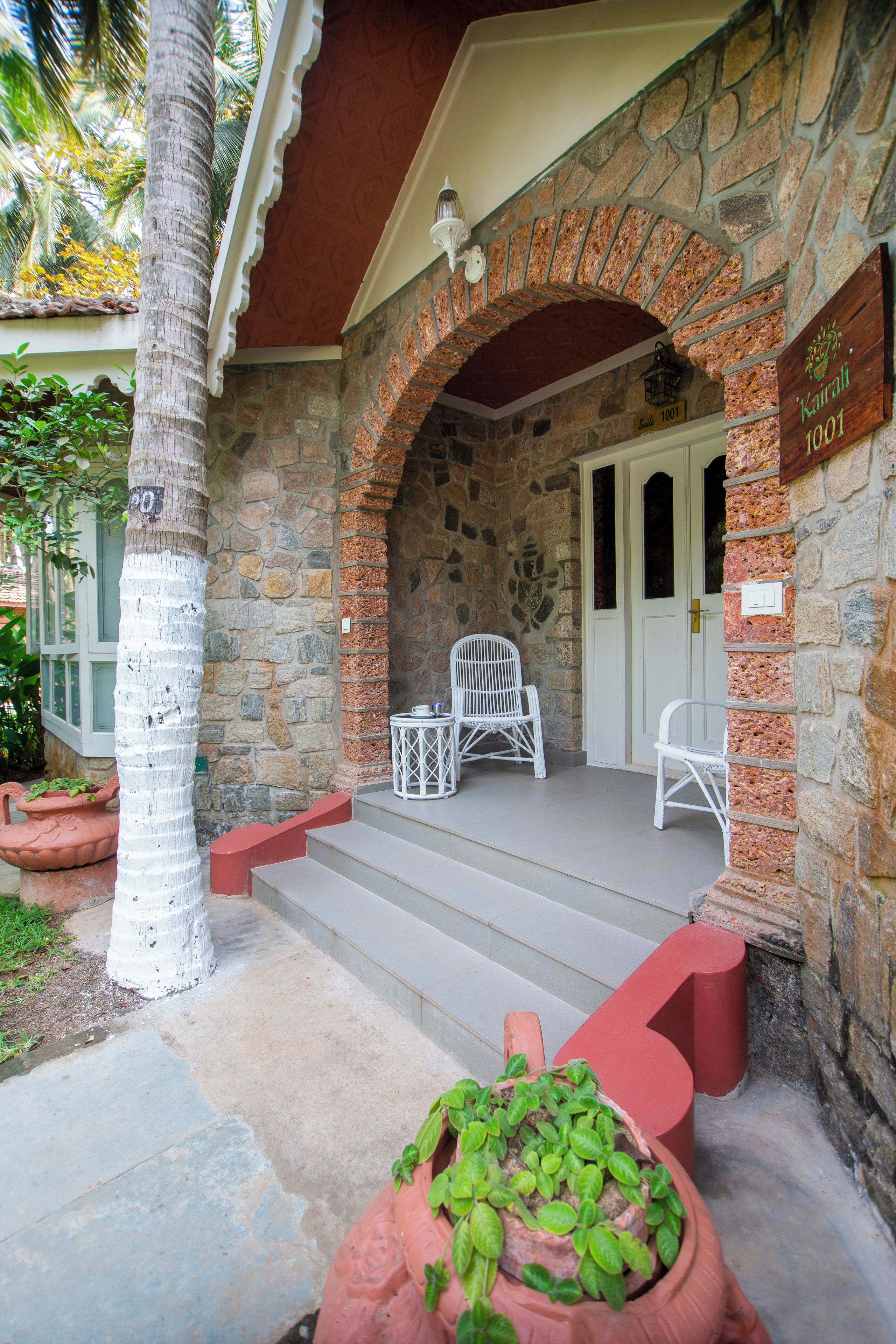 A stone building with a red door, a white chair, and a sign indicating 'Suite 1001'.