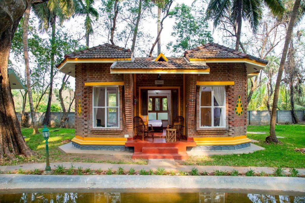 Una piccola casa in mattoni con tetto in tegole, un portico con due sedie e un tavolino.