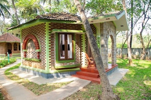 A small, brick building with a green and red facade, a wooden chair outside, and a stone pillar.