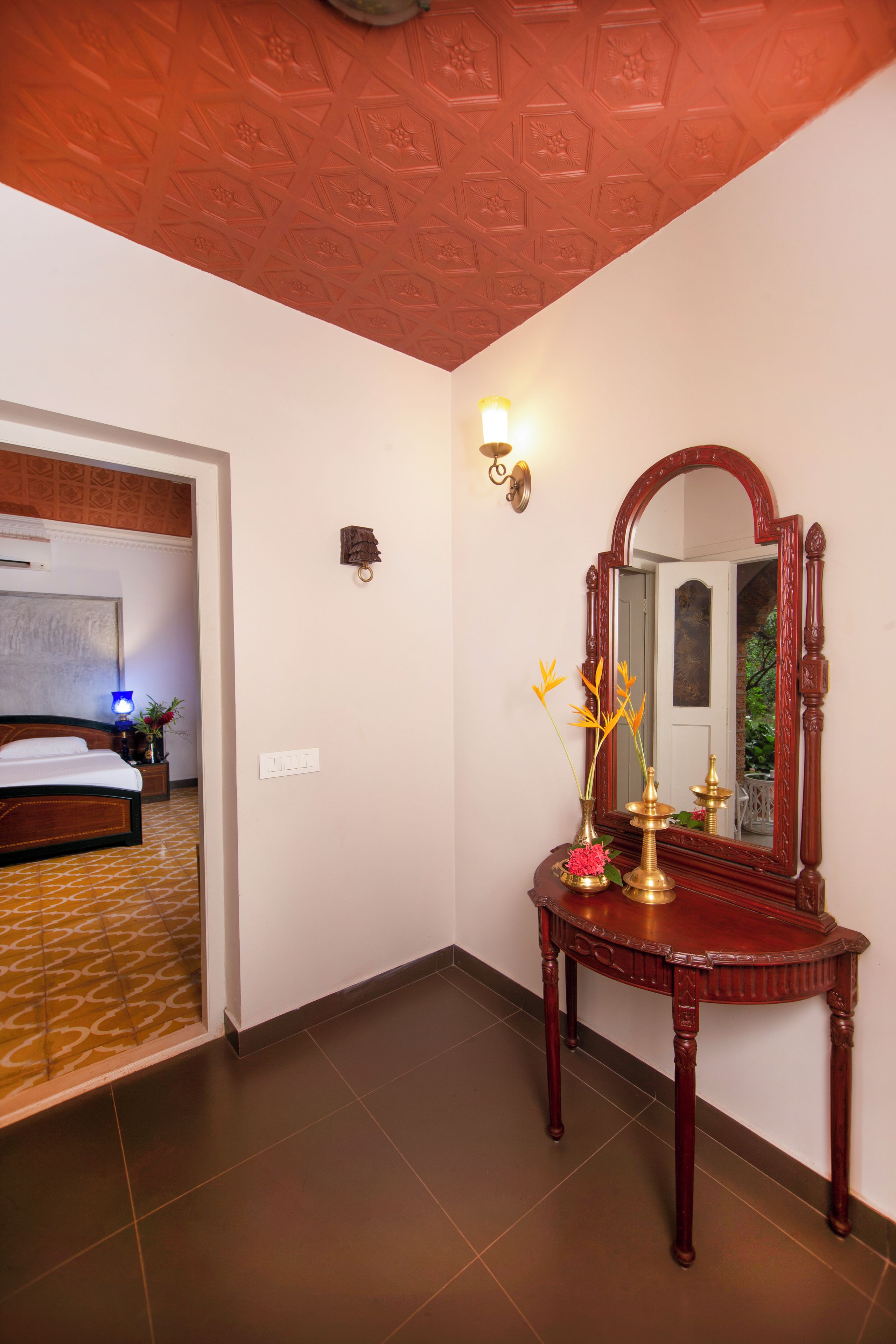 Een hotelkamer met een bed, een nachtkastje, een tafel met spiegel en een muur met lichtschakelaar.