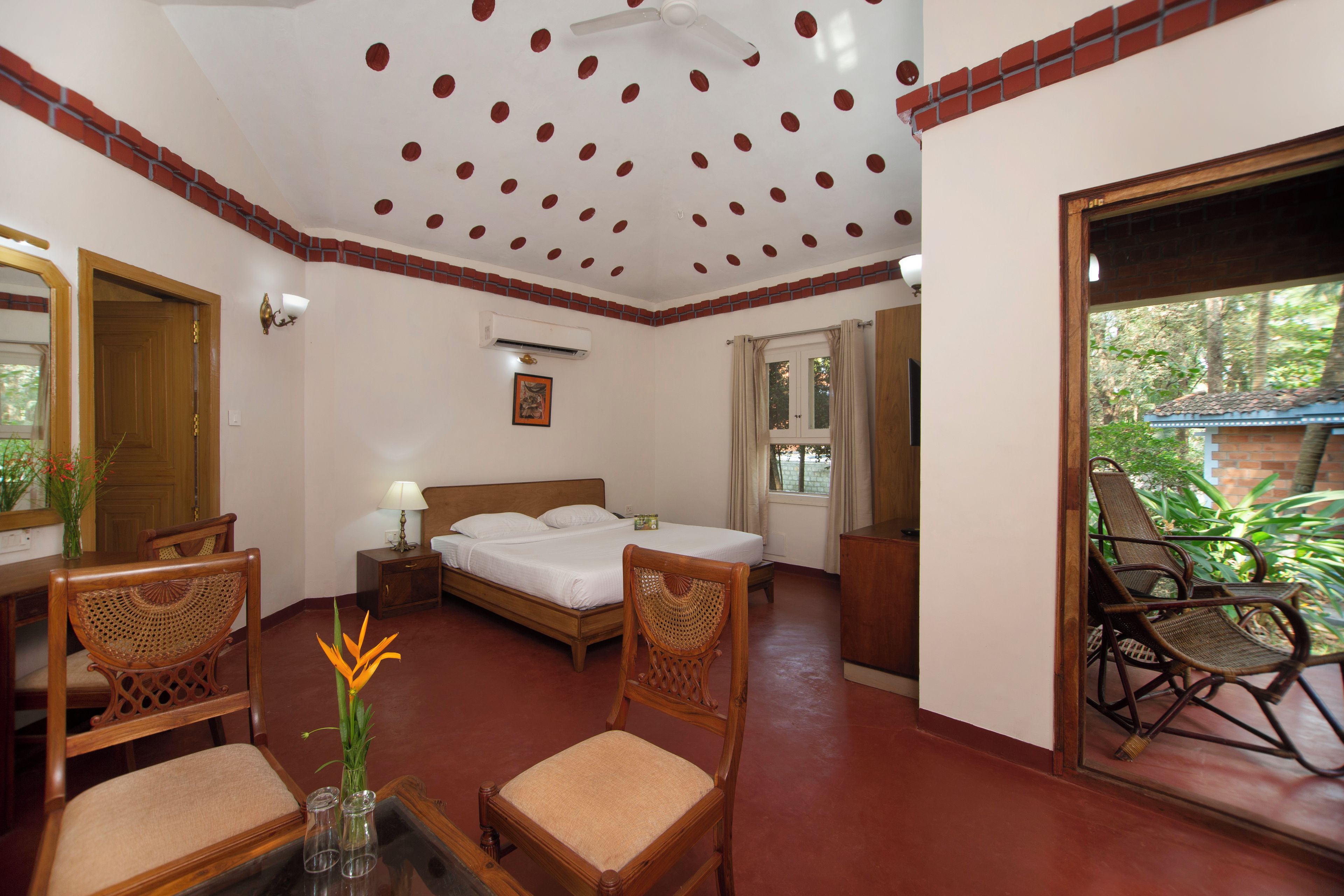 A hotel room with a bed, two wooden chairs, a table with a vase, and a view of greenery outside.
