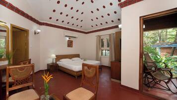 A hotel room with a bed, two wooden chairs, a table with a vase, and a view of greenery outside.