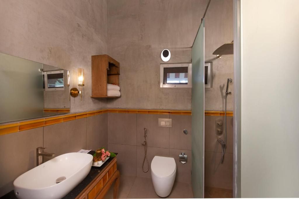 Een badkamer met een groot wit wastafel, toilet, een douche met glazen wanden en een spiegel met een houten plank erboven.